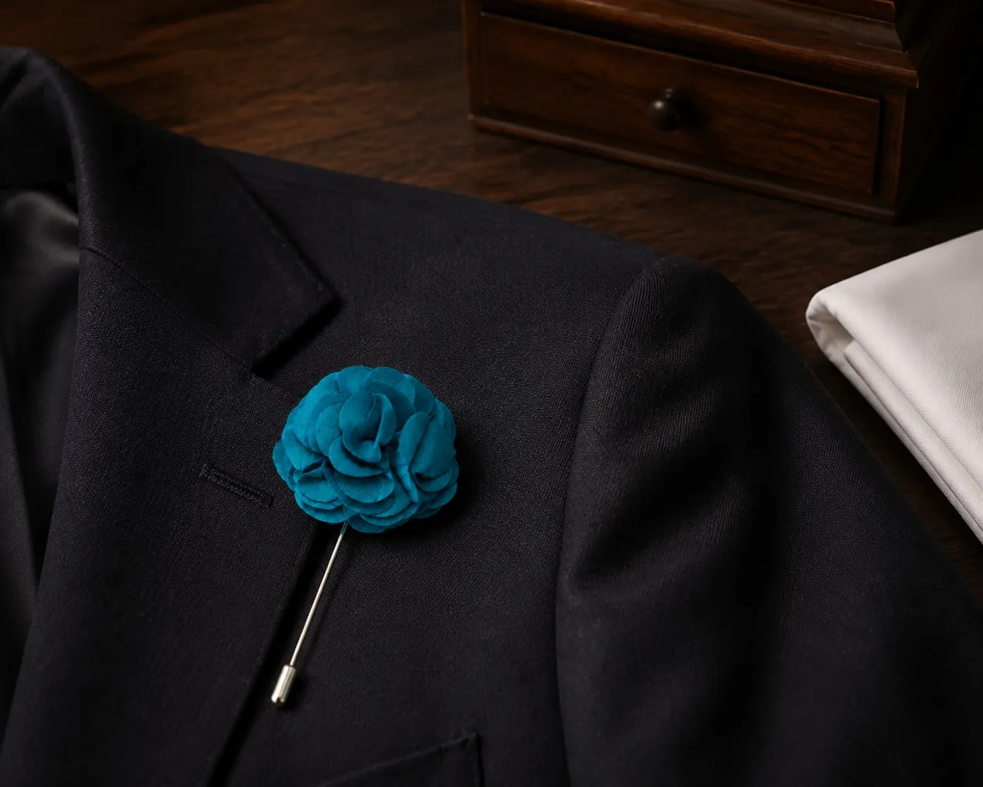 Pino de lapela em flor azul-turquesa, preso à lapela de um paletó preto