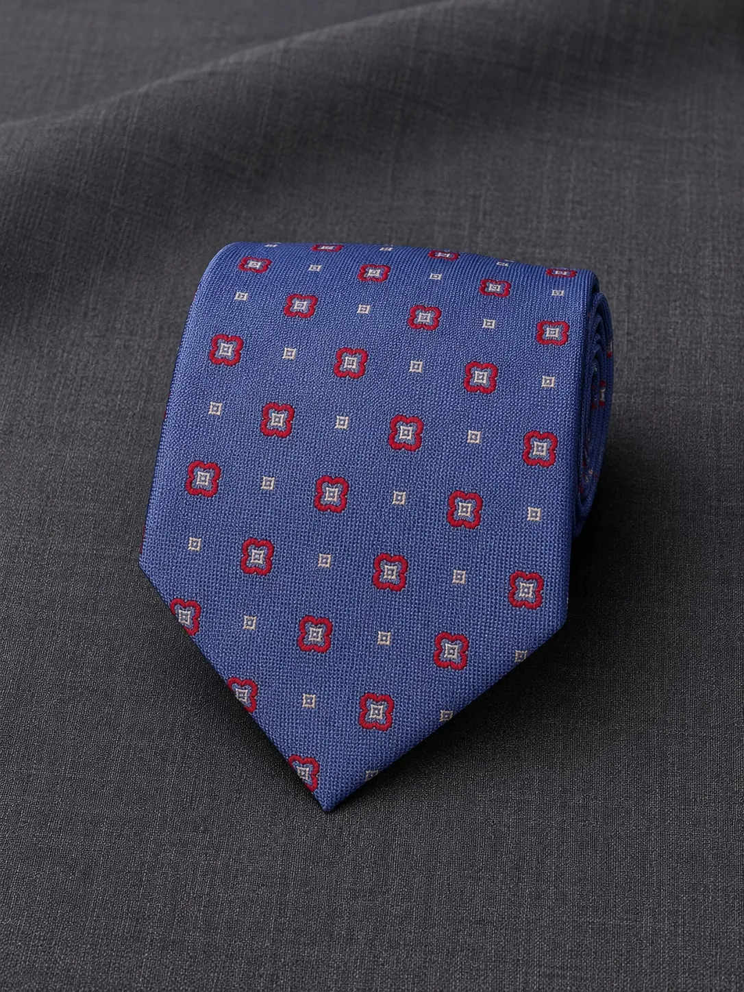 Gravata clássica azul-violeta com medalhões vermelhos e brancos, sobre tecido de terno