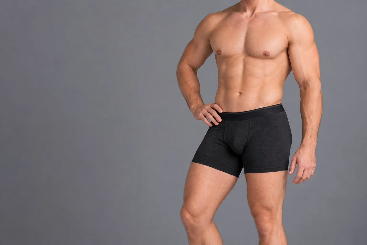 Homem de cueca boxer curta preta, de perfil, com a mão na cintura