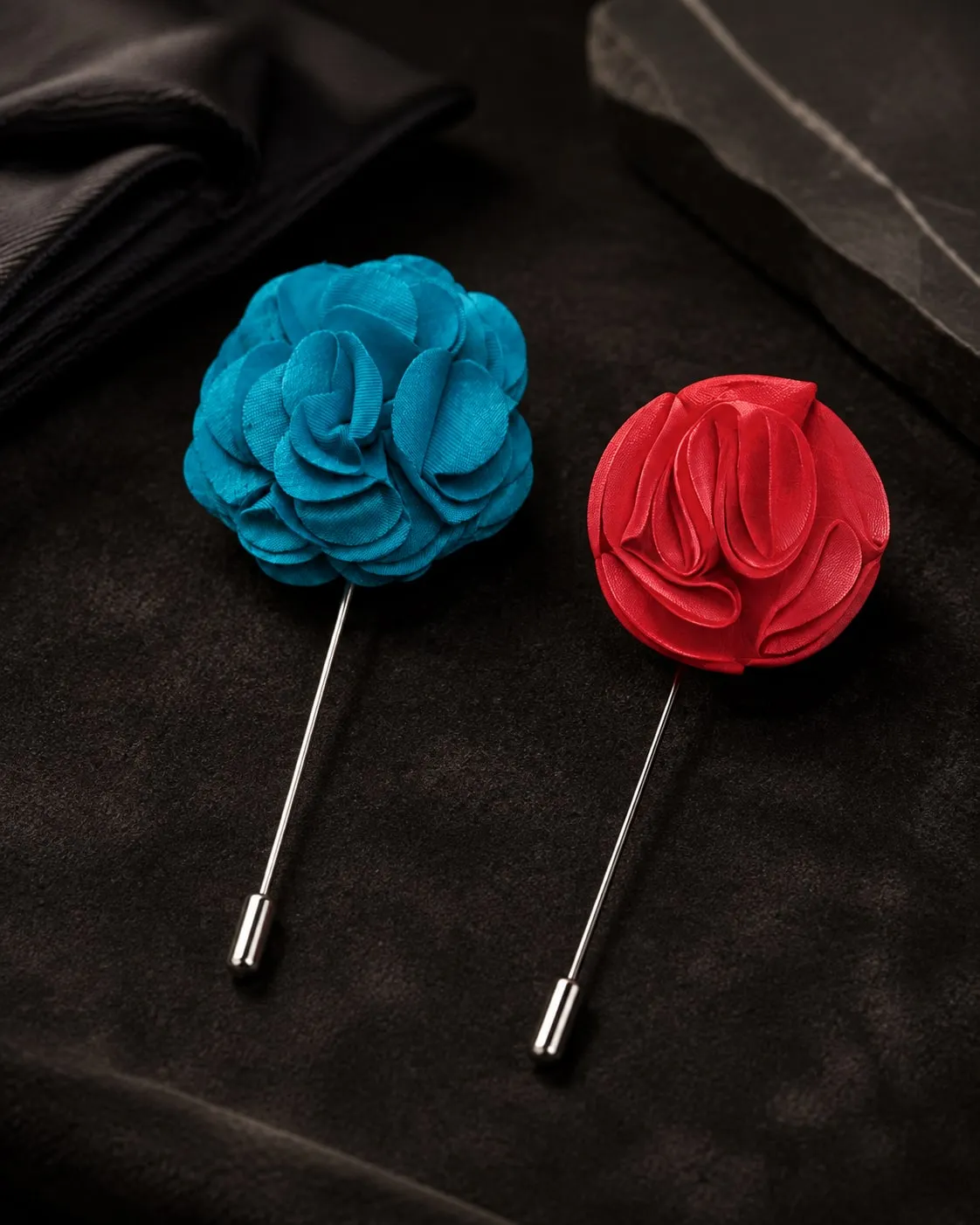 Dois pinos de lapela em flor de tecido, um azul-turquesa e outro vermelho